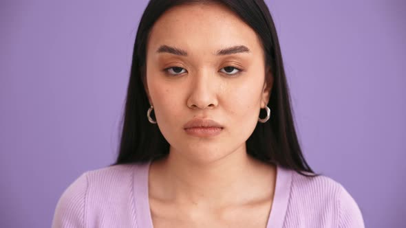 Concentrated Asian brunette woman wearing purple t-shirt looking at the camera