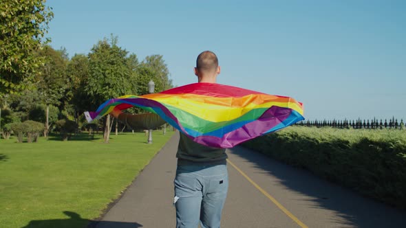 Confident Gay Man Walking Holding Rainbow Flag in Park