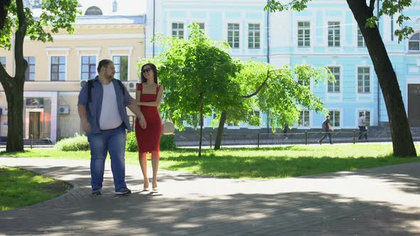 Beautiful Woman and Fat Man Holding Hands Walking in Park, Dream, Leisure Time