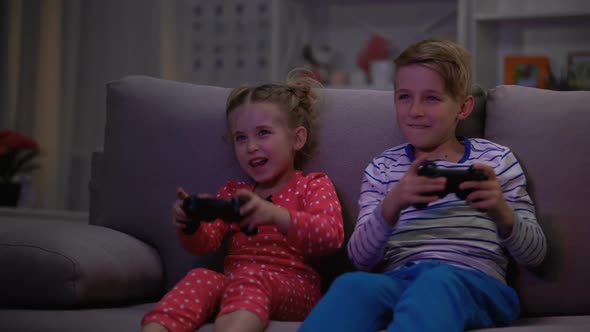 Happy Brother and Sister Playing Video Game at Night Sitting Sofa, Addiction