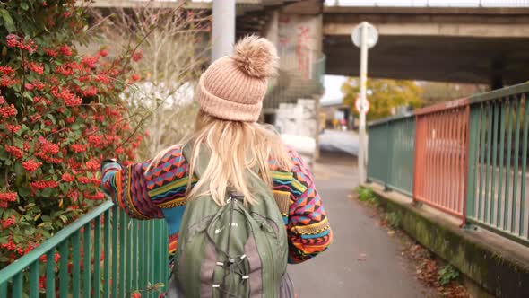 woman touching some berry bush as she walks by it and smiles into the camera afterwards