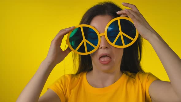 A Young Woman in Funny Yellow Hippie Sunglasses is Touching Her Hair