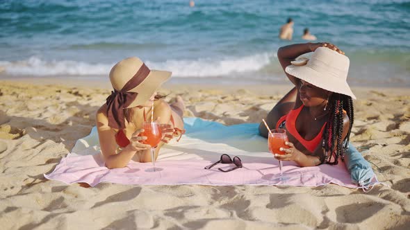 Two Girls Lying on Sandy Seashore in Straw Sun Hats