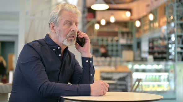 Old Man Talking on Smartphone in Cafe