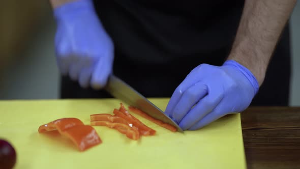 Close scene of cooking process. The cooker in gloves finely chopping red pepper on a board and add i