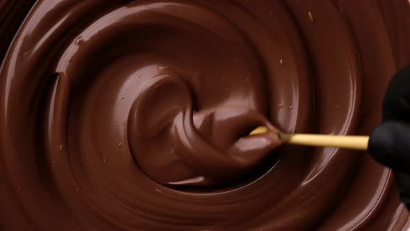 Hand stirring melted dark chocolate with golden spoon