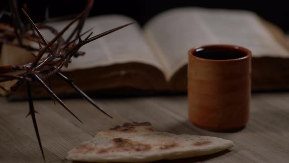 Ripped Bread Being Placed On Table With Cup Of Wine, Crown Of Thorns And Bible