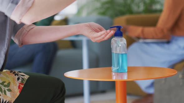 Mid section of woman sanitizing her hands at office