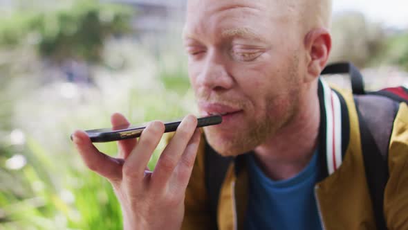 Happy albino african american man with dreadlocks in park talking on smartphone