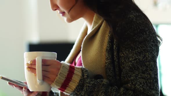 Woman having coffee while using mobile phone