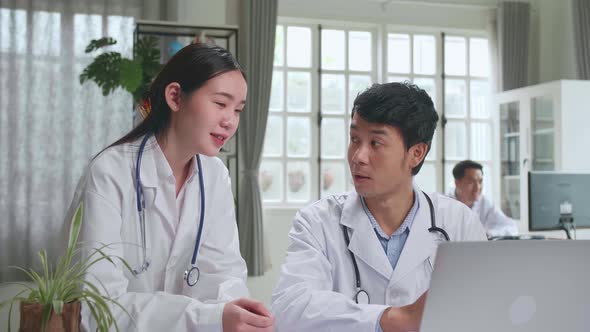 Two Asian Professional Physicians Talking, Consulting And Working On Laptop Computer