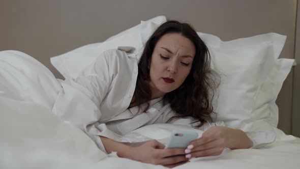 Upset Woman Is Reading Messages in Cell Phone at Morning Waking Up in Her Bed