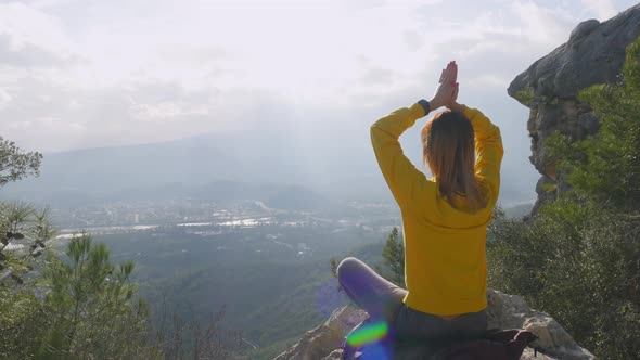 Young Woman Sitting in Yoga Pose on the End of the Cliff