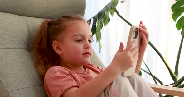 Cute Little Girl with Smartphone Sitting on Armchair Close Up