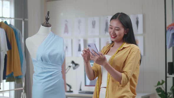 Female Designer Looking At A Dress On A Mannequin And Comparing It To The Pictures On Smartphone