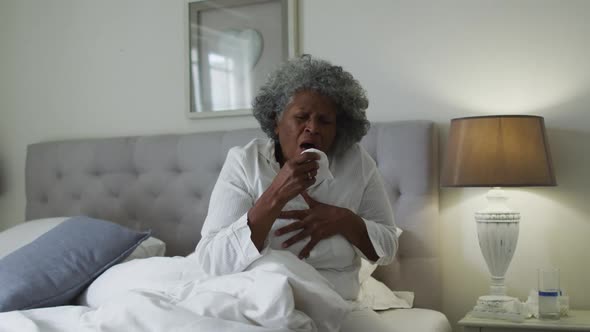 Sick senior african american woman coughing while sitting on the bed at home