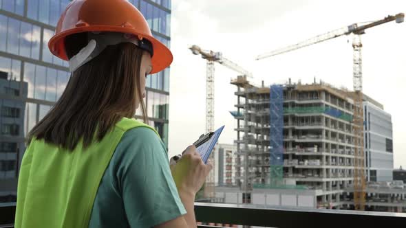 Young Female Builder in a Signal Vest and Helmet Writes Something