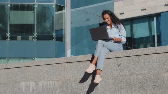 Long Shot Smiling Happy Young Business Woman Freelancer Girl Student Sitting on Street City Building