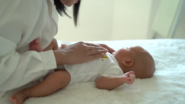 Cute Asian Newborn Baby Boy Lying on Bed and Mother Hands on Belly Indoors