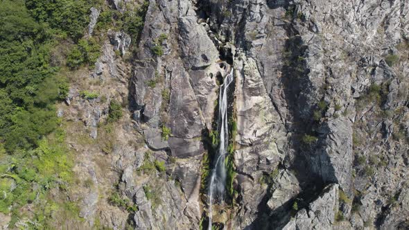 Water stream falling from rocky cliff, Frecha da Mizarela, Portugal, aerial descend view