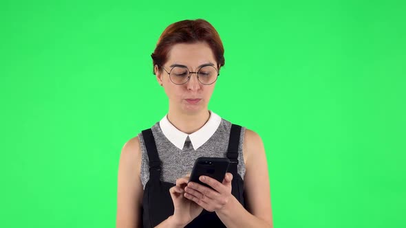 Portrait of Funny Girl in Round Glasses Is Texting on Her Phone. Green Screen