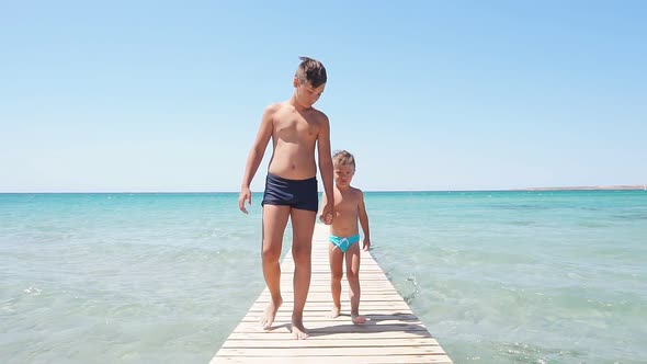 Children Walk Carelessly Along the Sea Pier on a Sunny Day, Two Brothers Holding Hands, Slow-motion