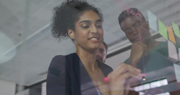 Diverse colleagues using memo notes and writing on glass wall having a discussion