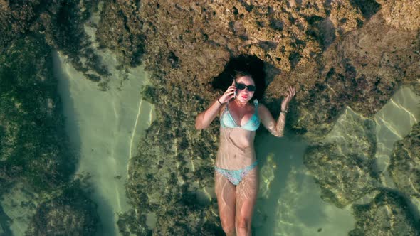 Aerial Footage of Female Person in Blue Bikini Talking on a Cell Phone While Laying on Natural Reef