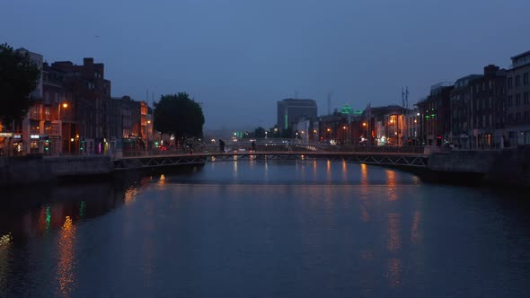 Pedestrians Walking on Footbridge Across River in Evening City