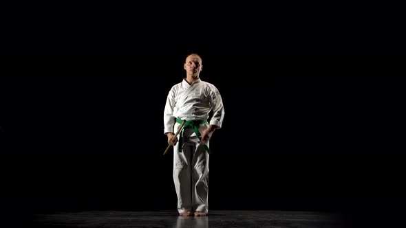 Kendo Fighter on White Kimono Practicing Martial Art with the Bamboo Bokken on Black Background.