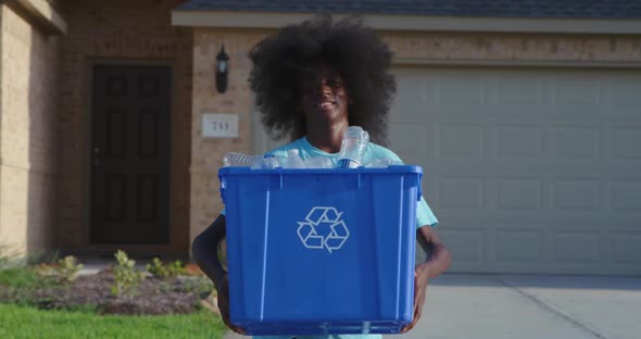 African American adolescents with huge Afro smiling as he hold recycle bin full of plastic bottles