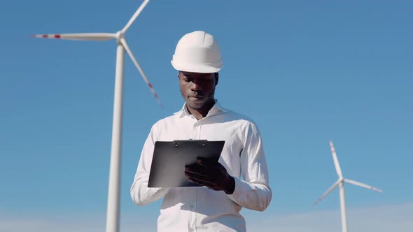 African American Electrician Engineer Standing Against the Backdrop of a Windmill at an Air Power