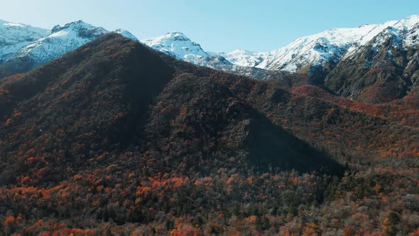 Aerial establishing shot of snowy mountains with autumn vegetation on base in Chile