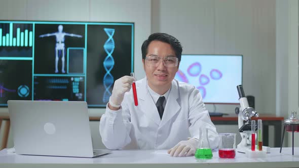 Asian Scientist Researching In The Laboratory With Test Tube, He Warmly Smiles Into The Camera