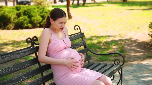 a Pregnant Girl Sits on a Park Bench and Her Stomach Begins To Hurt. Pregnant Woman Stroking and