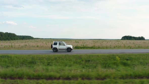 Aerial View of a Car Driving Along the Road Among Fields of Green Grass