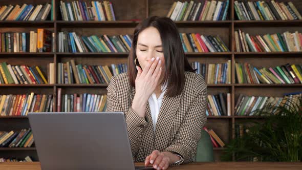 Tired Businesswoman in Brown Jacket Types on Grey Laptop