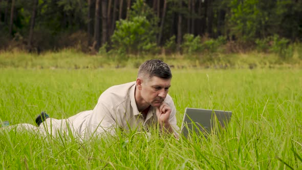 Businessman Works Behind a Laptop Lying on the Grass