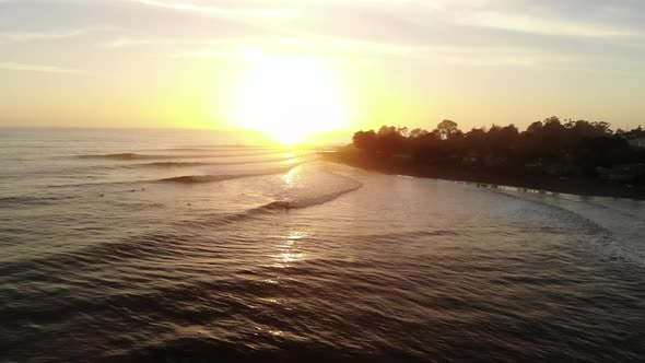 Aerial drone footage at Rincon Point surf break with waves and people surfing to the beach at sunset