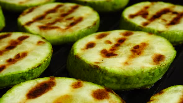 Fried zucchini slices rotate in a grill pan.