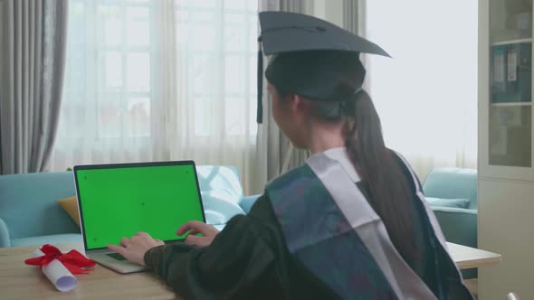 Asian Woman Wearing A Graduation Gown And Cap Use Laptop Computer With Green Mock-Up Screen