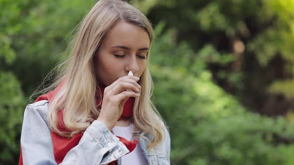 Young Woman Wearing Red Scarf Spraying Nasal Spray Standing in The City Park. Health Care Therapy