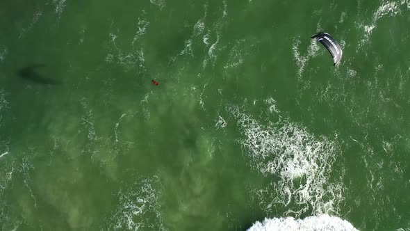 AERIAL: Top View Rotating Shot of Young People Kite Surfing Ride on Big Green Waves in Baltic Sea