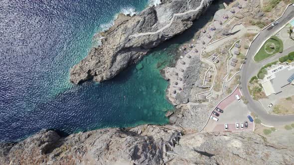 Drone flies over the rocky nature and blue sea with swimmers and boat in sight.