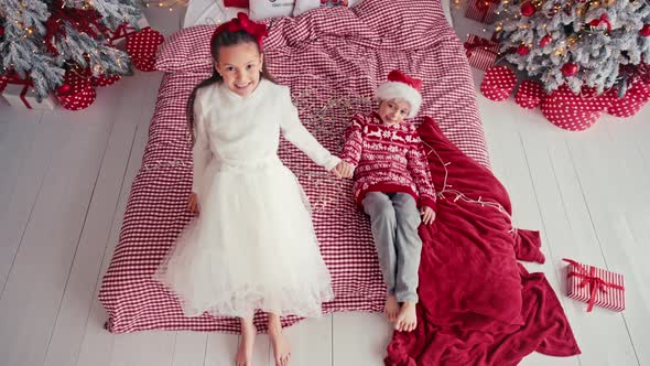 Portrait of Attractive Cute Kids Wearing Christmas Wear Falling Together on Bed in Apartment