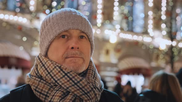 An Elderly Man Stands at a Christmas Market Next to a Shop Window Decorated with Bright Lights and