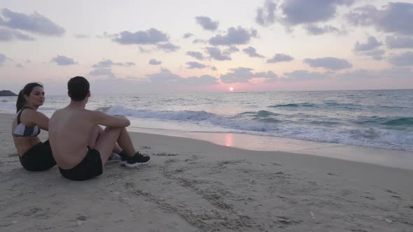 Young fit couple resting on beach after training at sunset