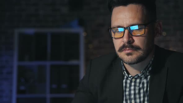 Portrait of Handsome Businessman in Glasses Working with Computer in Dark Office