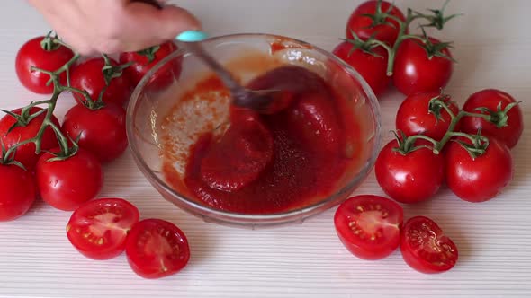 Closeup of a Woman Mixing Tomato Paste in a Bowl Lie Next to Fresh Tomatoes