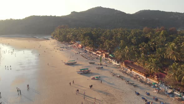 Low tide Palolem Beach at sunset with tourists enjoying the paradisiac ocean shore, in Goa, India